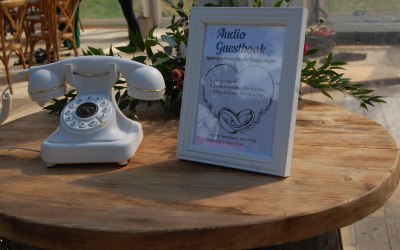 A white audio guestbook phone and white frame set up for a wedding. 